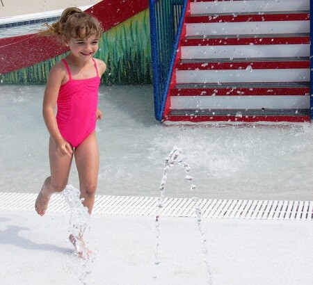 Smiling little girl in a pink swimsuit runs into the water at the Isle of Iberia RV Resort's splash pad in New Iberia.